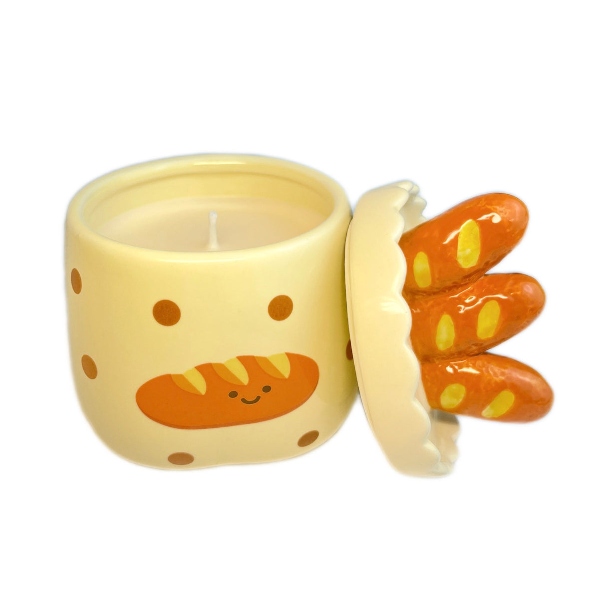 Baguette & butter scented candle in a ceramic jar with polka dots and a smiling baguette illustration, shown open with the baguette-shaped lid resting beside it on a white background.