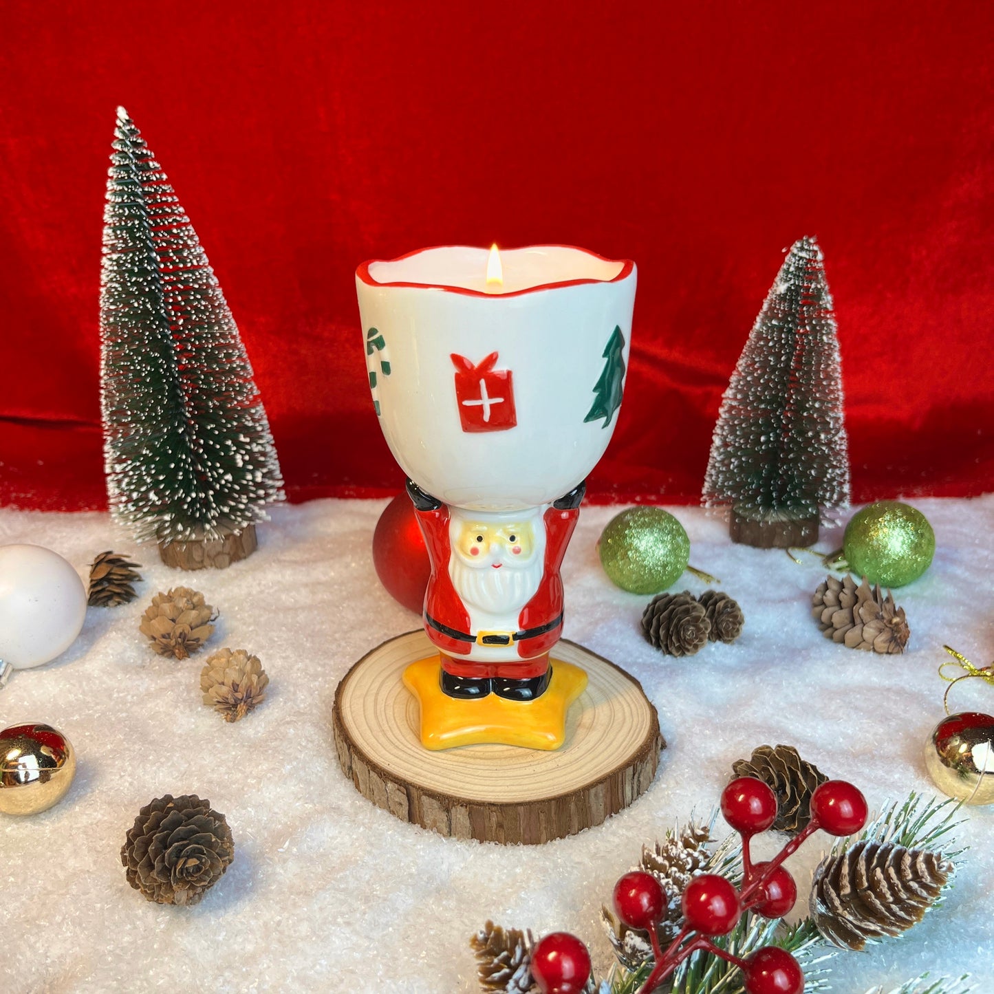 Spiced cranberry cider scented ceramic Santa goblet candle glowing in a festive Christmas scene with pinecones, ornaments, and snowy décor.