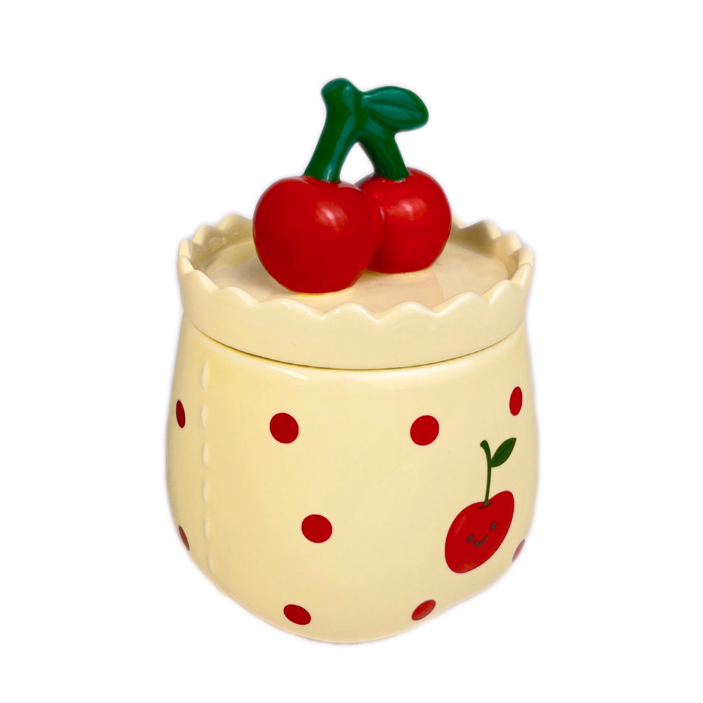 Velvet cherry scented candle in a ceramic jar with red polka dots and a smiling cherry illustration, topped with a cherry-shaped lid, photographed on a white background.